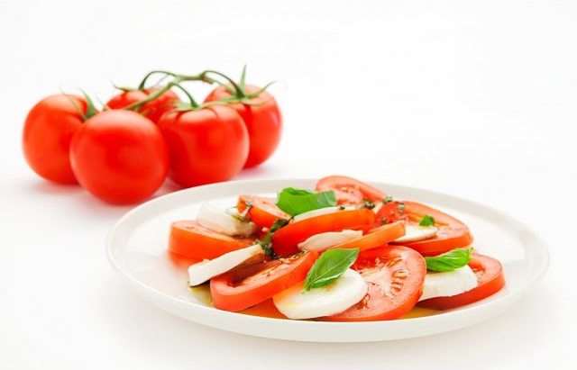 A white ceramic plate topped with slices of fresh tomatoes, bocconcini cheese, basil leaves and a drizzle of a maple olive oil and vinegar sauce